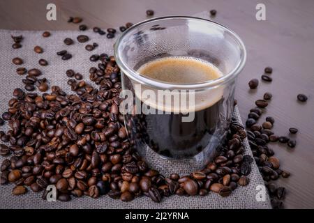 Glasbecher mit Kaffee und Haufen gerösteter Kaffeebohnen Stockfoto