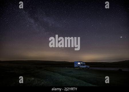 Einsam beleuchteter Wohnmobil, Wohnmobil bei Nacht unter Sternenhimmel, Milchstraße. Stockfoto