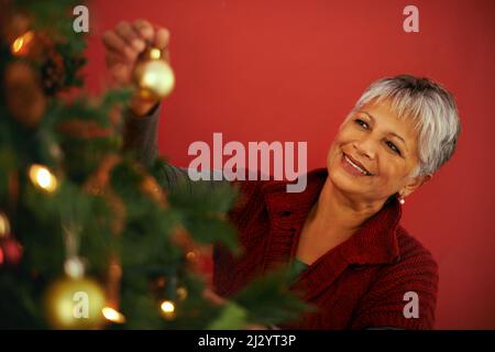 Der letzte Schliff am Baum. Ausgeschnittene Aufnahme einer reifen Frau, die einen weihnachtsbaum schmückt. Stockfoto