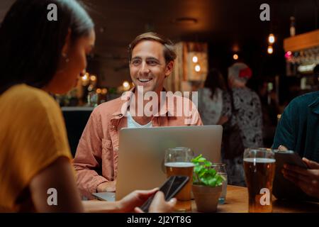 Diverse Kollegen, die mit einem Laptop im Restaurant Getränke trinken Stockfoto