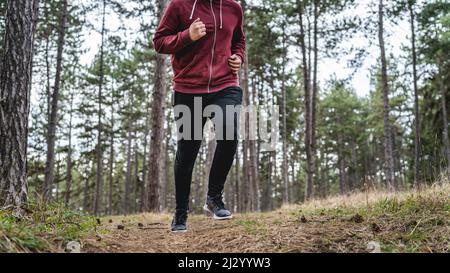 Seitenansicht Körper eines Mannes junger kaukasischer Rüde läuft durch den Wald in der Natur joggen im Herbst oder Frühling Tag - Sport Fitness und recreati Stockfoto