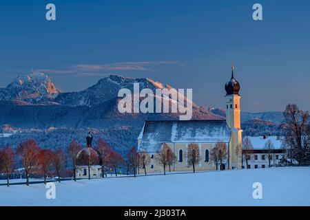 Schneebedeckte Wiesen mit Wilteling-Kirche und Bergen des Wendelsteingebietes im Hintergrund, Irschenberg, Oberbayern, Bayern, Deutschland Stockfoto