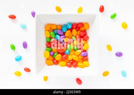 Eine Schüssel mit Gelee-Bohnen auf weißem Hintergrund. Einige Jelly-Bohnen sind um die Schüssel verstreut. Stockfoto