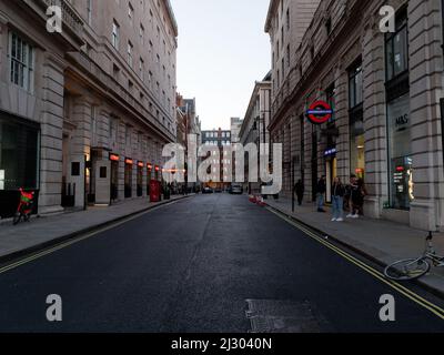 London, Greater London, England, 12 2022. März: Straße vor Piccadilly am Abend mit Neonlicht links und einem U-Bahn-Schild rechts. Stockfoto