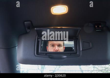 Mann im Spiegel / Mann in einem Kosmetikspiegel auf einem Auto Sonnenblende / Fahrzeug Sonnenschutz Stockfoto