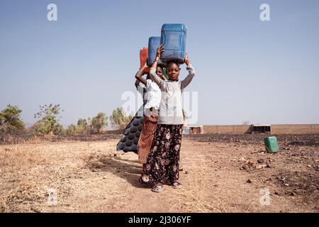 Kleine Prozession von Mädchen in der ländlichen afrikanischen Landschaft, die sich mit dem Transport von Trinkwasser aus der fernen Bohrung in ihr Dorf beschäftigten Stockfoto