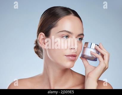 Shes bekam immer Hautpflege im Kopf. Kurzer Schuss einer attraktiven jungen Frau, die mit einem Behälter mit Feuchtigkeitscreme vor grauem Hintergrund posiert. Stockfoto
