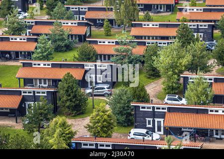 Ferienbungalow Park mit identischen Hütten in symmetrischer Reihenfolge in grüner Waldgegend. Holzchalets mit orangefarbenen Dachziegeln in Gras und Büschen. N Stockfoto