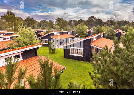 Ferienbungalow Park mit identischen Hütten in symmetrischer Reihenfolge in grüner Waldgegend. Holzchalets mit orangefarbenen Dachziegeln in Gras und Büschen. N Stockfoto