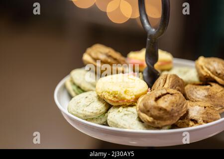 Auf einem abgestuften Serviertablett mit verschwommenem Licht im Hintergrund werden verschiedene Makronen-Aromen angeboten. Stockfoto