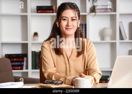 Junge asiatische Tutor in Ohrhörern zu Hause sitzen Stockfoto