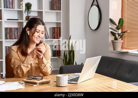 Junge asiatische Tutor in Ohrhörern zu Hause sitzen Stockfoto