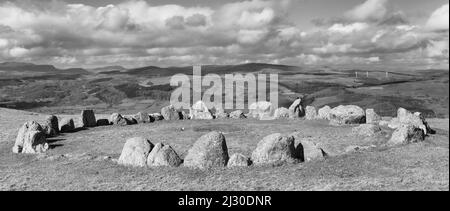 Eine Graustufenansicht des Moel Ty Uchaf Steinkreises und entfernter Windkraftanlagen, North Wales, Vereinigtes Königreich Stockfoto