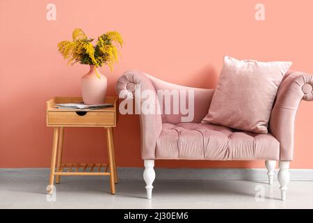 Vase mit Mimosenblumen auf Tisch und Sofa im Innenraum des Zimmers Stockfoto