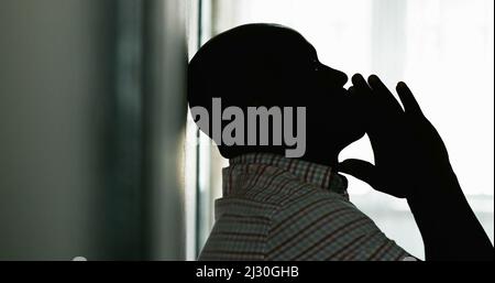 Beunruhigender schwarzer Mann, der in Angst an die Wand gelehnt ist, Silhouette einer afrikanischen Person in Verzweiflung Stockfoto