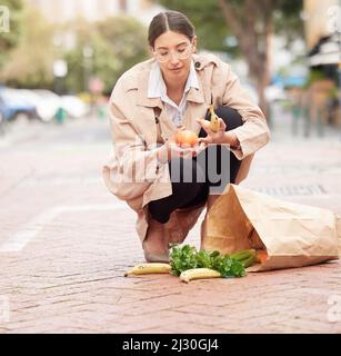 Vielleicht ist es Zeit für ein Auto. Aufnahme einer jungen Frau, die überwältigt aussaht, während sie Lebensmittel vom Boden abholt. Stockfoto