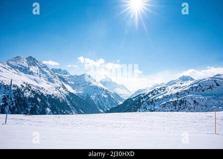 Malerische Aussicht auf die strahlende Sonne durch den blauen Himmel über schneebedeckten Bergen Stockfoto