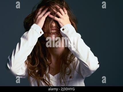 Unordentliche Haare sind egal. Studioaufnahme einer unkenntlichen Frau, die ihr Gesicht mit ihren Haaren vor blauem Hintergrund bedeckt. Stockfoto