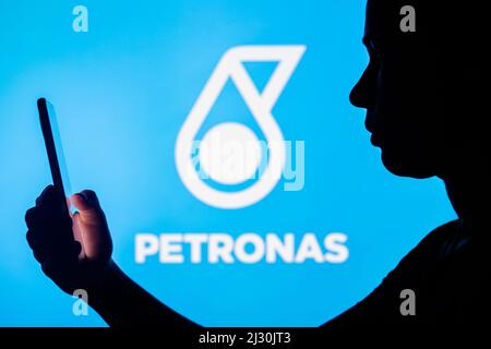 In dieser Fotobilder hält die Silhouette einer Frau ein Smartphone mit dem Petronas-Logo im Hintergrund. Stockfoto