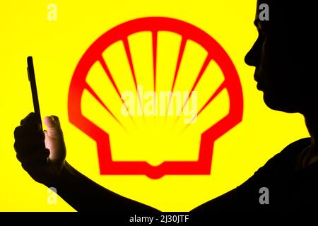 In dieser Fotobilder hält die Silhouette einer Frau ein Smartphone mit dem Shell-Logo im Hintergrund. Stockfoto