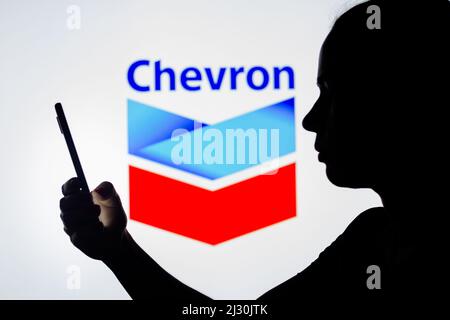 In dieser Fotobilder hält die Silhouette einer Frau ein Smartphone mit dem Chevron-Logo im Hintergrund. Stockfoto