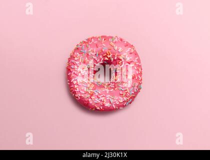 Pinkfarbener, glasierter Donut mit Besprengung auf pastellrosa Hintergrund Stockfoto