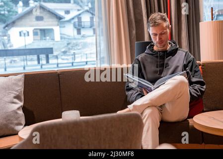 Mann, der sich auf der Couch entspannt, während er in der Lounge des Resorts ein Magazin liest Stockfoto