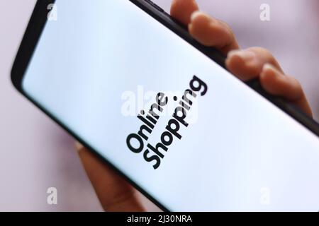 Eine vertikale Aufnahme einer Hand, die ein Smartphone mit einem Text auf dem Bildschirm hält, der „Online-Shopping“ besagt Stockfoto