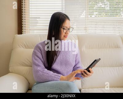 Asiatisches Mädchen mit Brille, Kopfhörer und Pflanzen, die von zu Hause aus mit einem Laptop und Handy arbeiten. Stockfoto