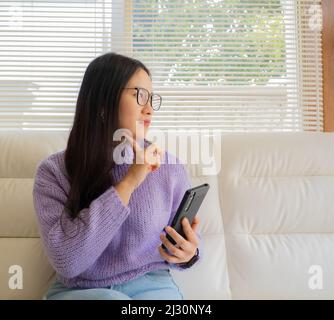 Asiatisches Mädchen mit Brille, Kopfhörer und Pflanzen, die von zu Hause aus mit einem Laptop und Handy arbeiten. Stockfoto