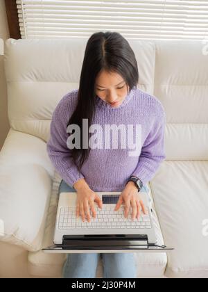 Asiatisches Mädchen mit Brille, Kopfhörer und Pflanzen, die von zu Hause aus mit einem Laptop und Handy arbeiten. Stockfoto