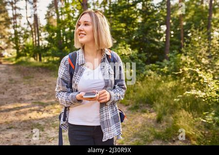 Frau navigieren mit dem Mobiltelefon, während sie während der Sommerwanderung im Wald spazieren geht Stockfoto
