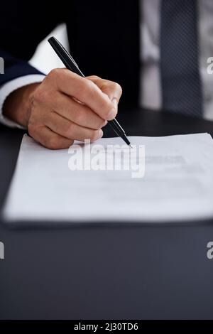 Alles sieht in Ordnung aus. Nahaufnahme eines Geschäftsmannes, der einen Vertrag unterzeichnet, während er an einem Schreibtisch in einem Büro sitzt. Stockfoto