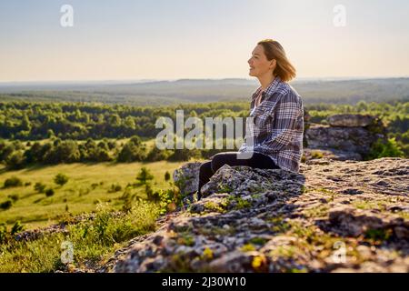 Entspannte Wanderin auf Felsen sitzend und die Landschaft genießend Stockfoto