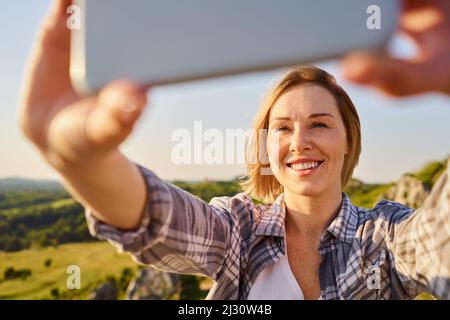 Nahaufnahme einer jungen Frau, die während einer sonnigen Sommerwanderung Selfie auf dem Land macht Stockfoto
