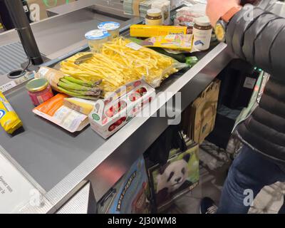 Karlsruhe, Deutschland - 12. März 2022: Seitenansicht des Mannes, der mehrere Lebensmittel arrangiert Süßigkeiten Gemüseobst Konfitüren auf dem Ladentisch im Supermarkt - Lebensmitteleinkäufe Stockfoto