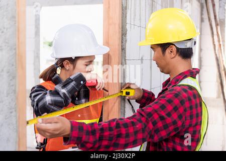 Männliche industrielle Bauarbeiter Installationsprozess Messung Holztür mit Maßband und Service Frau Überprüfung in Baustelle. Stockfoto