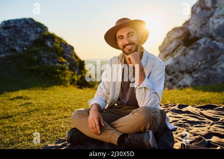 Porträt eines glücklichen jungen Mannes, der während einer Sommerwanderung im Jura in Polen auf einer Decke in den Bergen sitzt Stockfoto