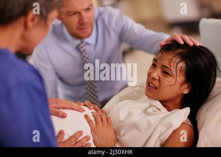 Gebären kann hart sein, aber so sind Sie. Aufnahme einer jungen Frau, die im Hintergrund mit ihrem Mann gebärt wurde, der sie unterstützt. Stockfoto