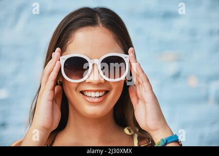 Shades on und bereit für den Sommer. Das verkürzte Porträt einer attraktiven jungen Frau, die ihre Sommertöne draußen vor einem blauen Hintergrund trägt. Stockfoto