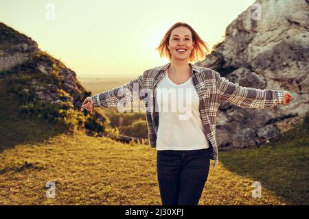 Glückliche, unbeschwerte Frau, die Sommerwanderung in den Bergen genießt, mit ausgestreckten Armen geht Stockfoto