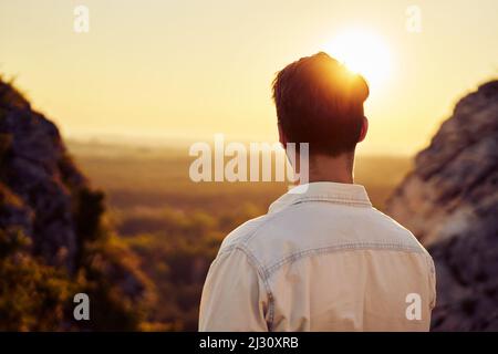 Rücken eines Mannes, der den Sonnenuntergang beim Wandern in den Bergen beobachtet Stockfoto