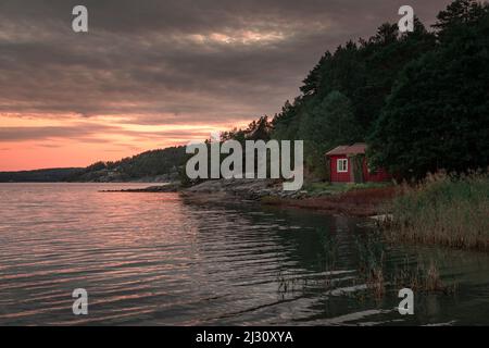 Rote Hütte am See mit Schilf auf der Insel des Orust-Archipels an der Westküste Schwedens bei Sonnenuntergang Stockfoto