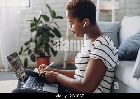 Profilporträt einer konzentrierten afroamerikanischen Frau, die zu Hause auf dem Boden sitzt und einen Laptop benutzt. Online-Kommunikation. Geschäftskommunikation Stockfoto