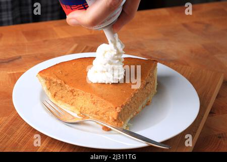 Ein Stück Kürbiskuchen mit Schlagsahne auf einem Holztisch Stockfoto