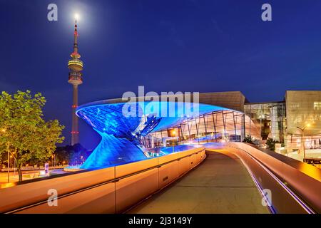 Blau beleuchtetes BMW Welt Gebäude mit dem Olympiaturm im Hintergrund, München, Oberbayern, Bayern, Deutschland Stockfoto