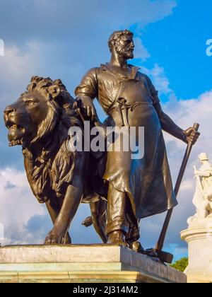 Ein Schmied und ein Löwe stellen eine „Herstellung“ an einer Ecke des Fußes des Queen Victoria Memorial vor dem Buckingham Palace in London, England, dar. Stockfoto