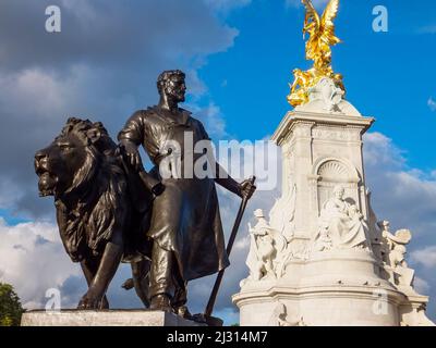 Ein Schmied und ein Löwe stellen eine „Herstellung“ an einer Ecke des Fußes des Queen Victoria Memorial vor dem Buckingham Palace in London, England, dar. Stockfoto