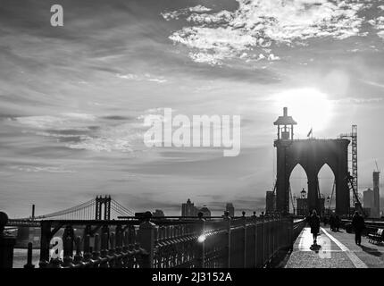 Sihouette einer Frau im Mantel, die im frühen Morgenlicht über die Brooklyn Bridge läuft Stockfoto