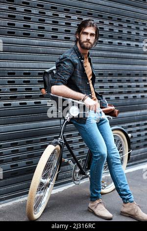 HES ist definitiv ein Trendsetter. Ganzkörperaufnahme eines hübschen jungen Mannes, der auf einem Fahrrad im Freien sitzt. Stockfoto